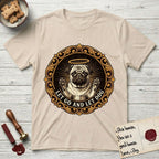 Let Go and Let Dog Pug T-Shirt flat lay in Sand, featuring a baroque medallion engraving of a haloed Pug with paws raised, framed in gold scrollwork.
