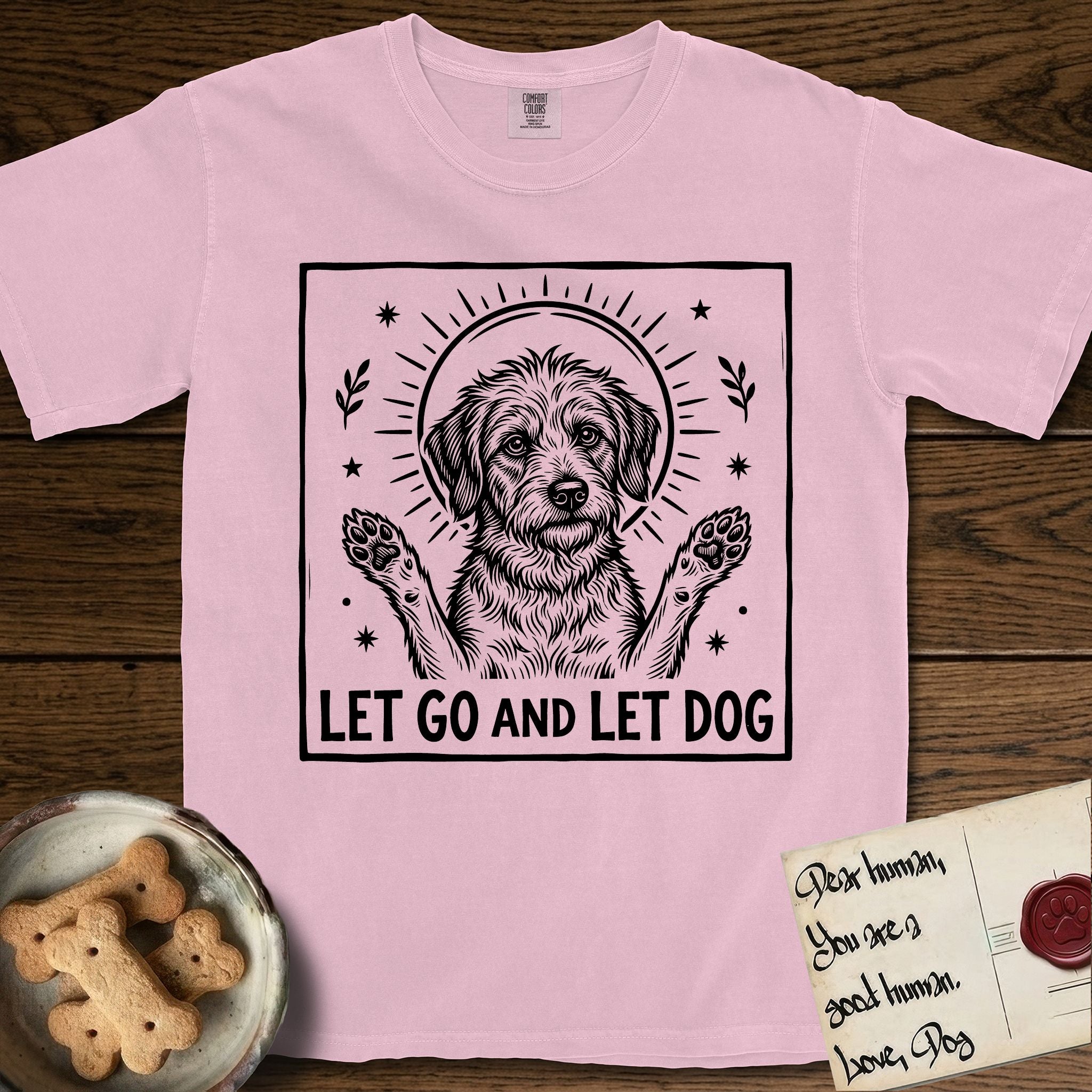 Let Go and Let Dog Rescue Mutt T-Shirt flat lay in Blossom, featuring a bold black-and-white woodcut of a haloed scruffy rescue mutt with both front paws raised.