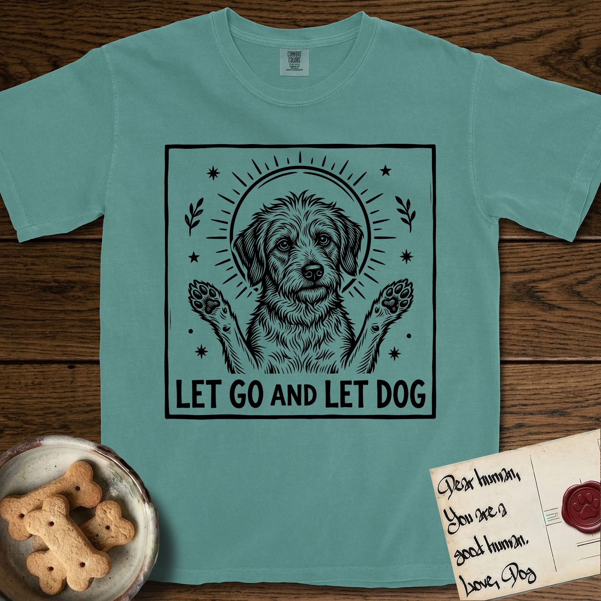 Let Go and Let Dog Rescue Mutt T-Shirt flat lay in Blue Spruce, featuring a bold black-and-white woodcut of a haloed scruffy rescue mutt with both front paws raised.