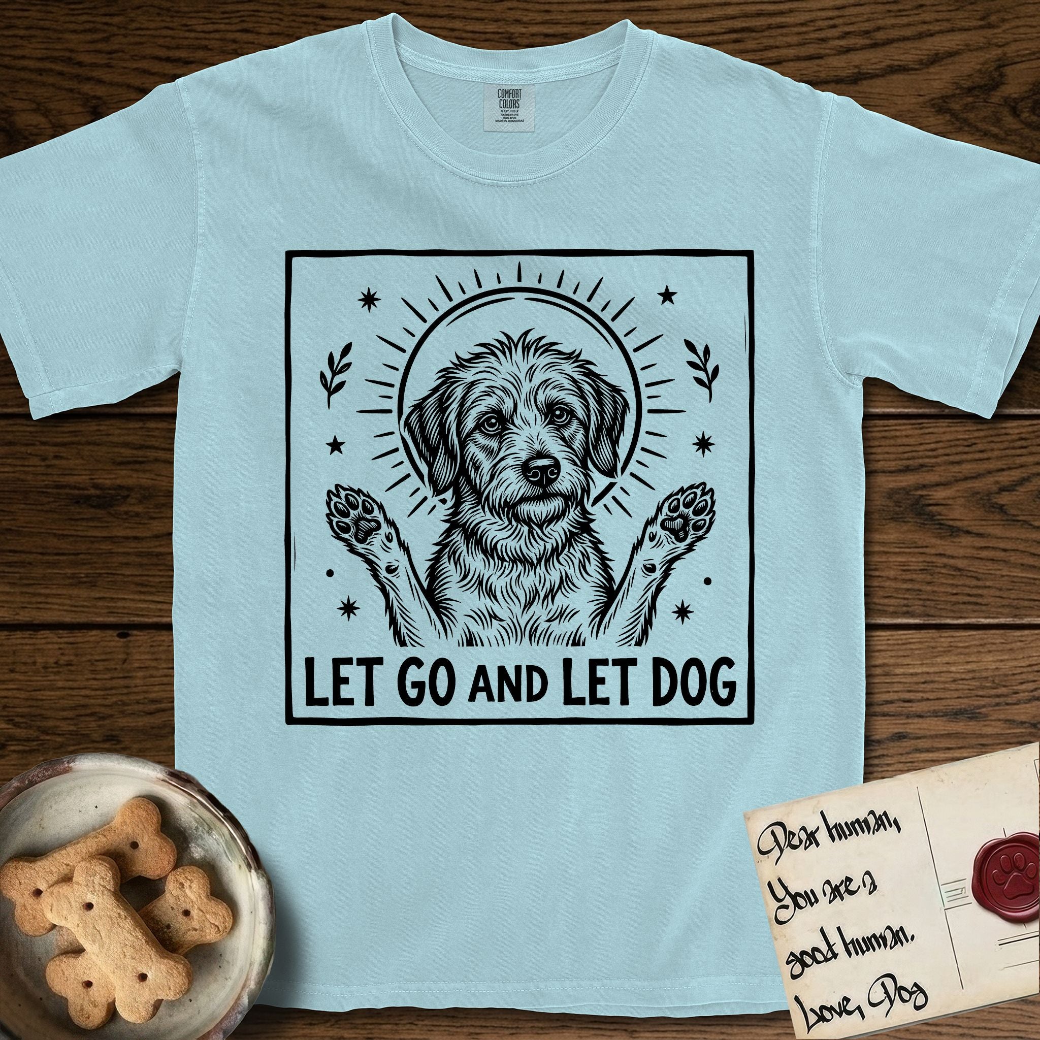 Let Go and Let Dog Rescue Mutt T-Shirt flat lay in Chambray, featuring a bold black-and-white woodcut of a haloed scruffy rescue mutt with both front paws raised.