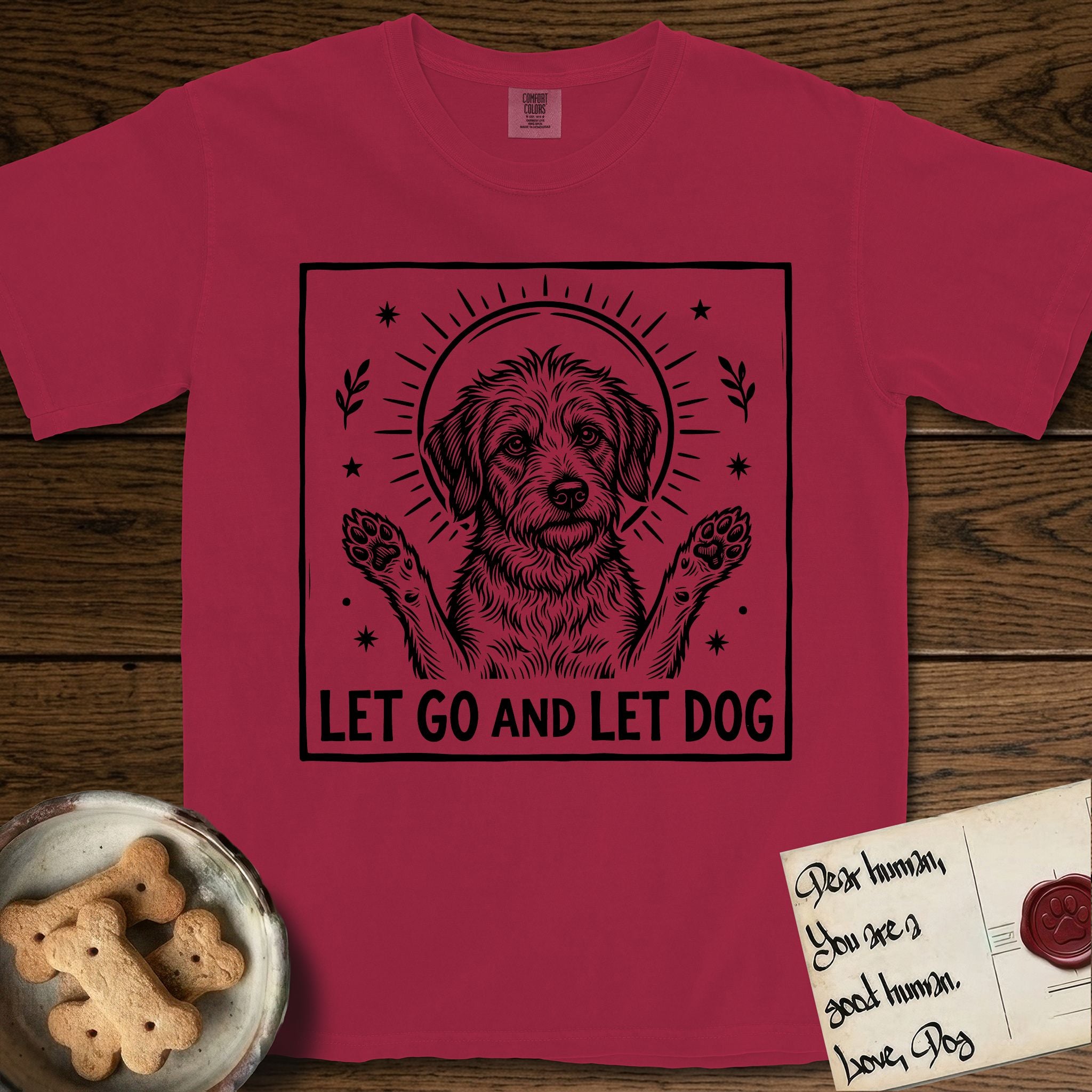 Let Go and Let Dog Rescue Mutt T-Shirt flat lay in Chili, featuring a bold black-and-white woodcut of a haloed scruffy rescue mutt with both front paws raised.