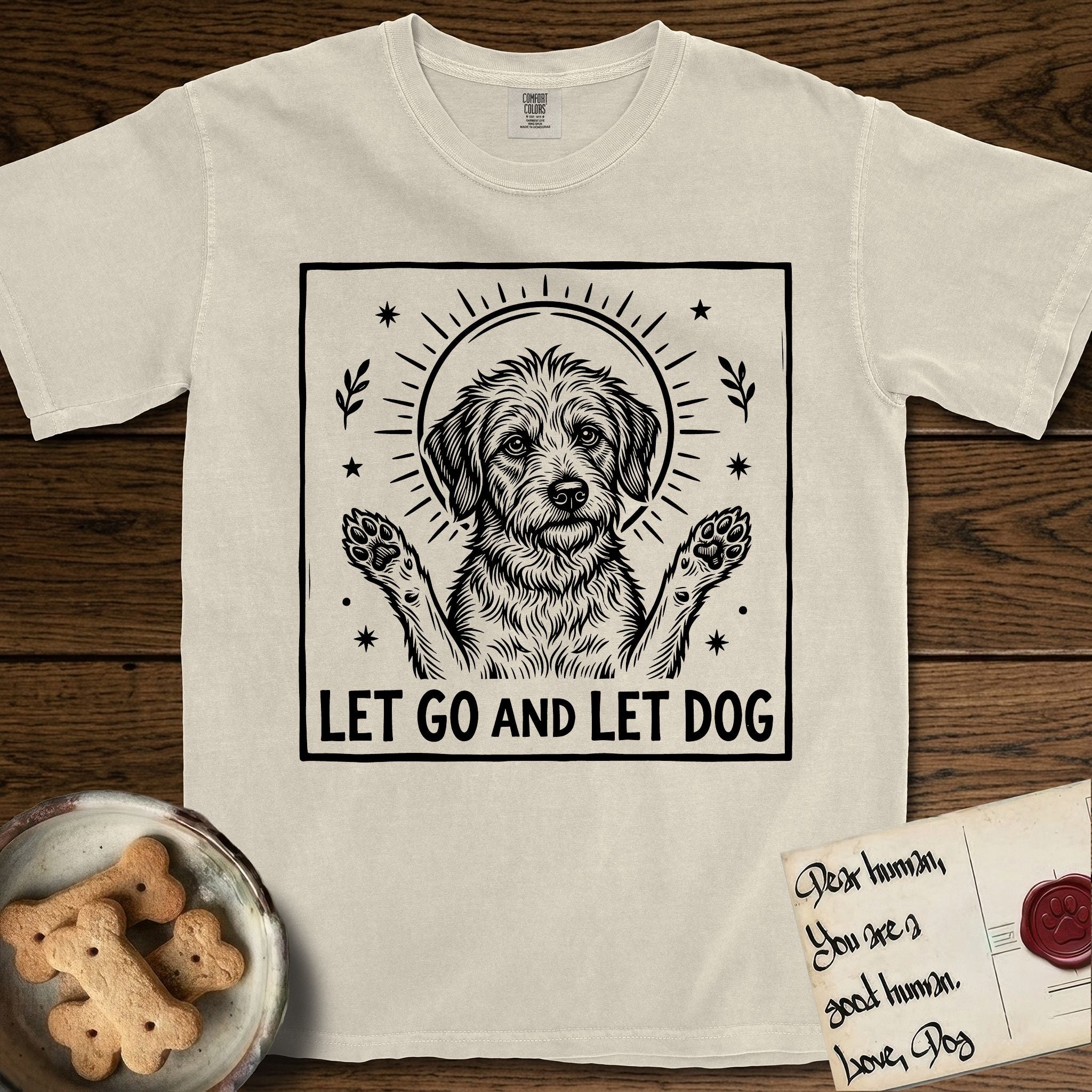 Let Go and Let Dog Rescue Mutt T-Shirt flat lay in Ivory, featuring a bold black-and-white woodcut of a haloed scruffy rescue mutt with both front paws raised.