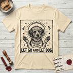 Let Go and Let Dog Rescue Mutt T-Shirt flat lay in Natural, featuring a bold black-and-white woodcut of a haloed scruffy rescue mutt with both front paws raised.