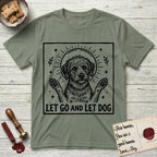 Let Go and Let Dog Rescue Mutt T-Shirt flat lay in Sage, featuring a bold black-and-white woodcut of a haloed scruffy rescue mutt with both front paws raised.