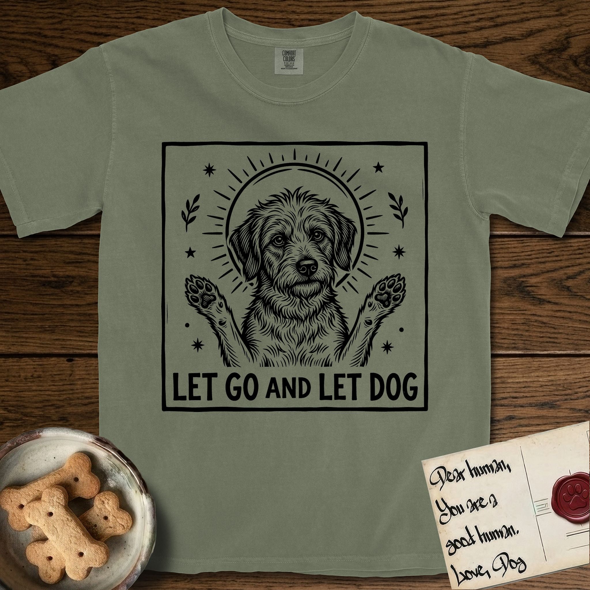 Let Go and Let Dog Rescue Mutt T-Shirt flat lay in Sage, featuring a bold black-and-white woodcut of a haloed scruffy rescue mutt with both front paws raised.