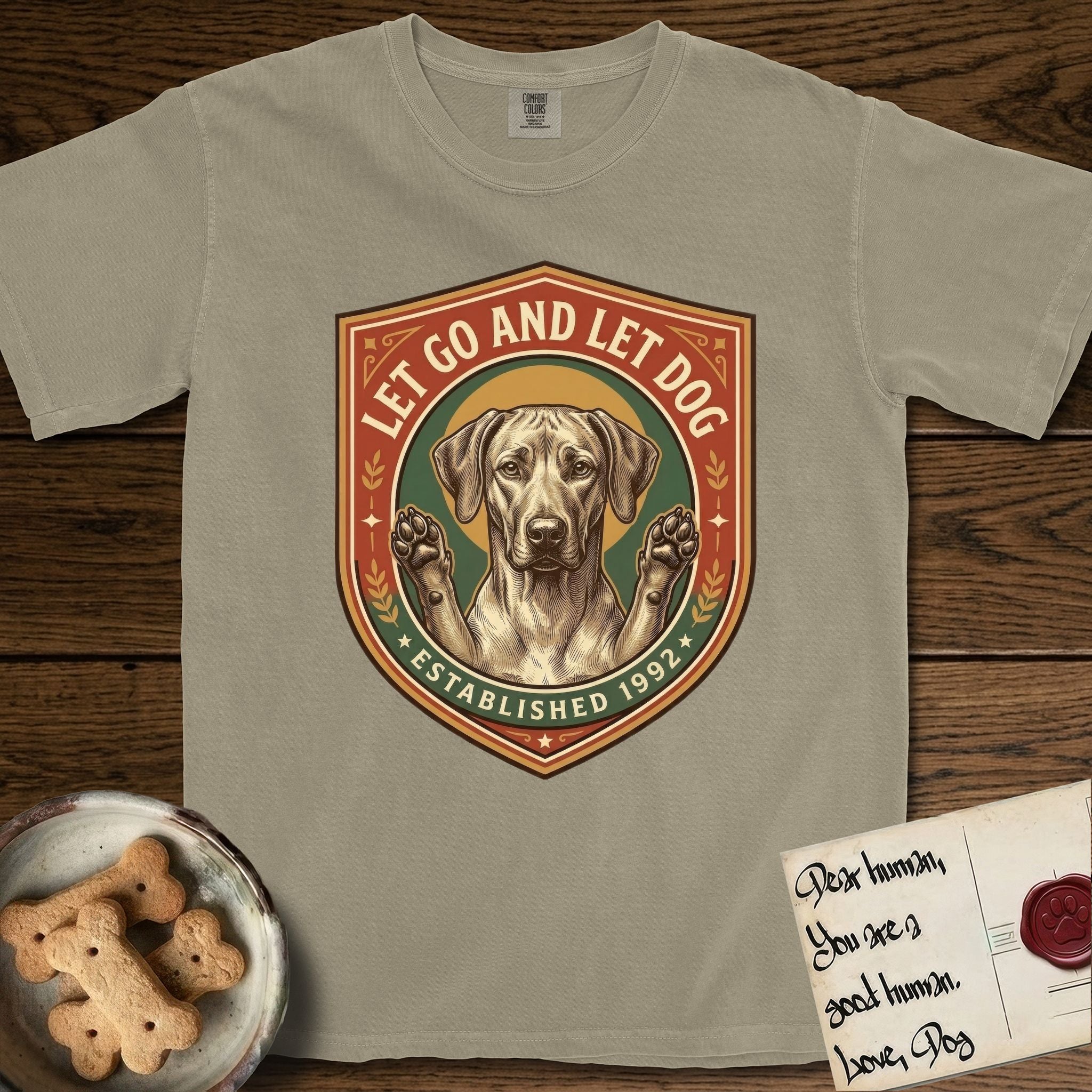 Let Go and Let Dog Rhodesian Ridgeback T-Shirt flat lay in Khaki, featuring a vintage engraved crest of a haloed Rhodesian Ridgeback with front paws raised.