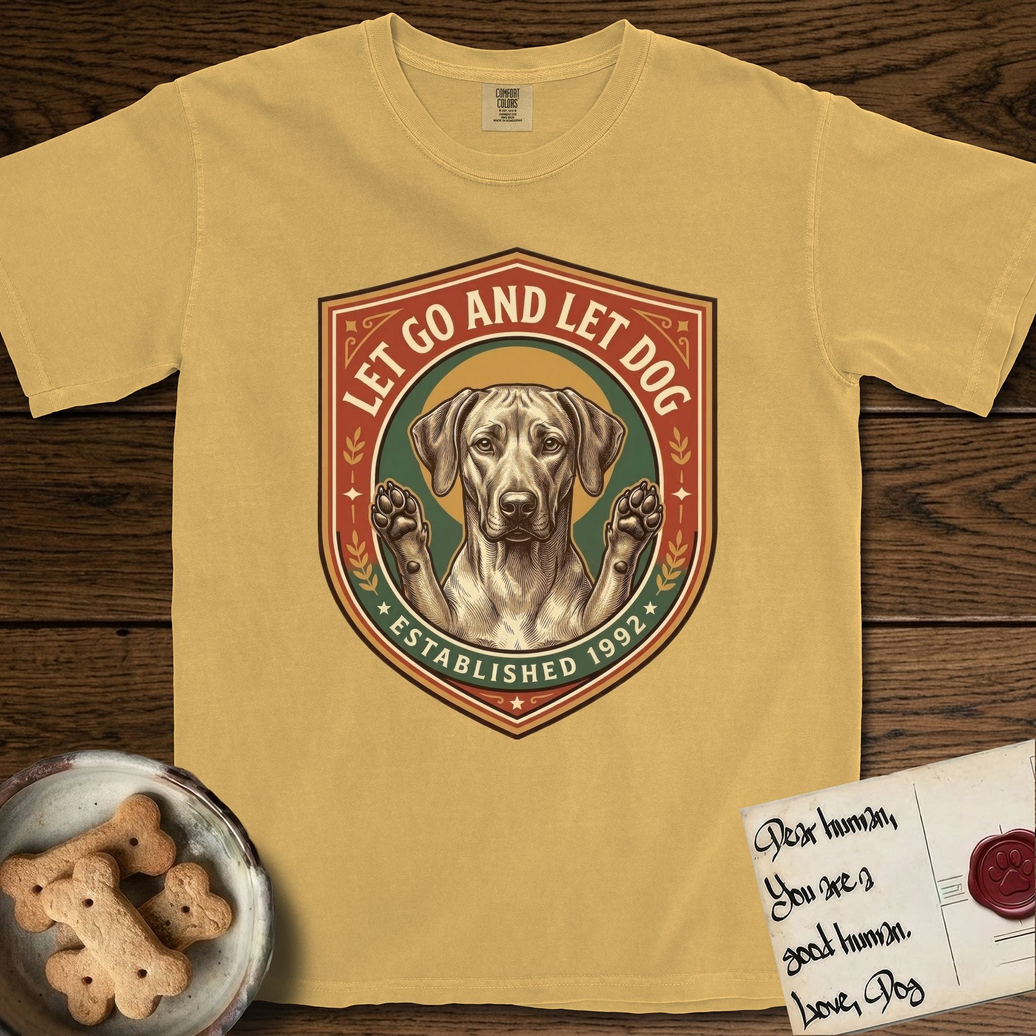 Let Go and Let Dog Rhodesian Ridgeback T-Shirt flat lay in Mustard, featuring a vintage engraved crest of a haloed Rhodesian Ridgeback with front paws raised.
