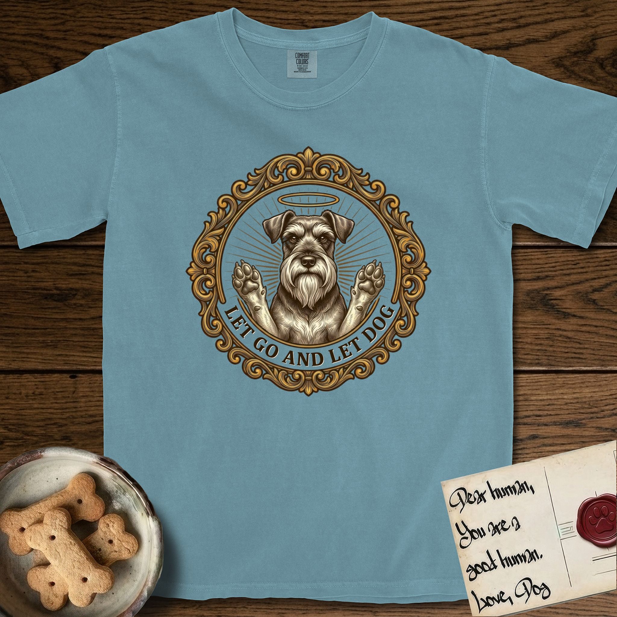 Let Go and Let Dog Schnauzer T-Shirt flat lay in Ice Blue, featuring an ornate gilded medallion of a haloed Schnauzer with front paws raised.