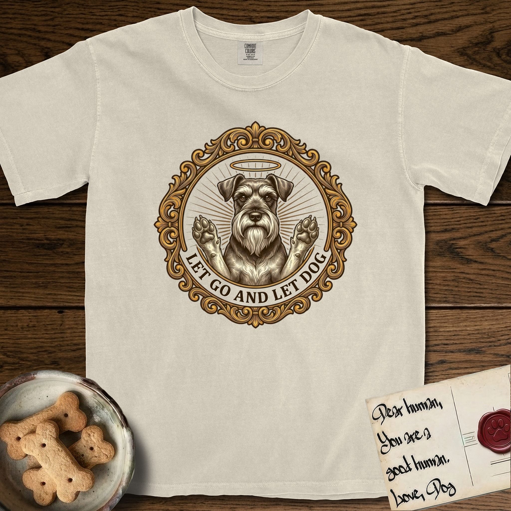 Let Go and Let Dog Schnauzer T-Shirt flat lay in Ivory, featuring an ornate gilded medallion of a haloed Schnauzer with front paws raised.