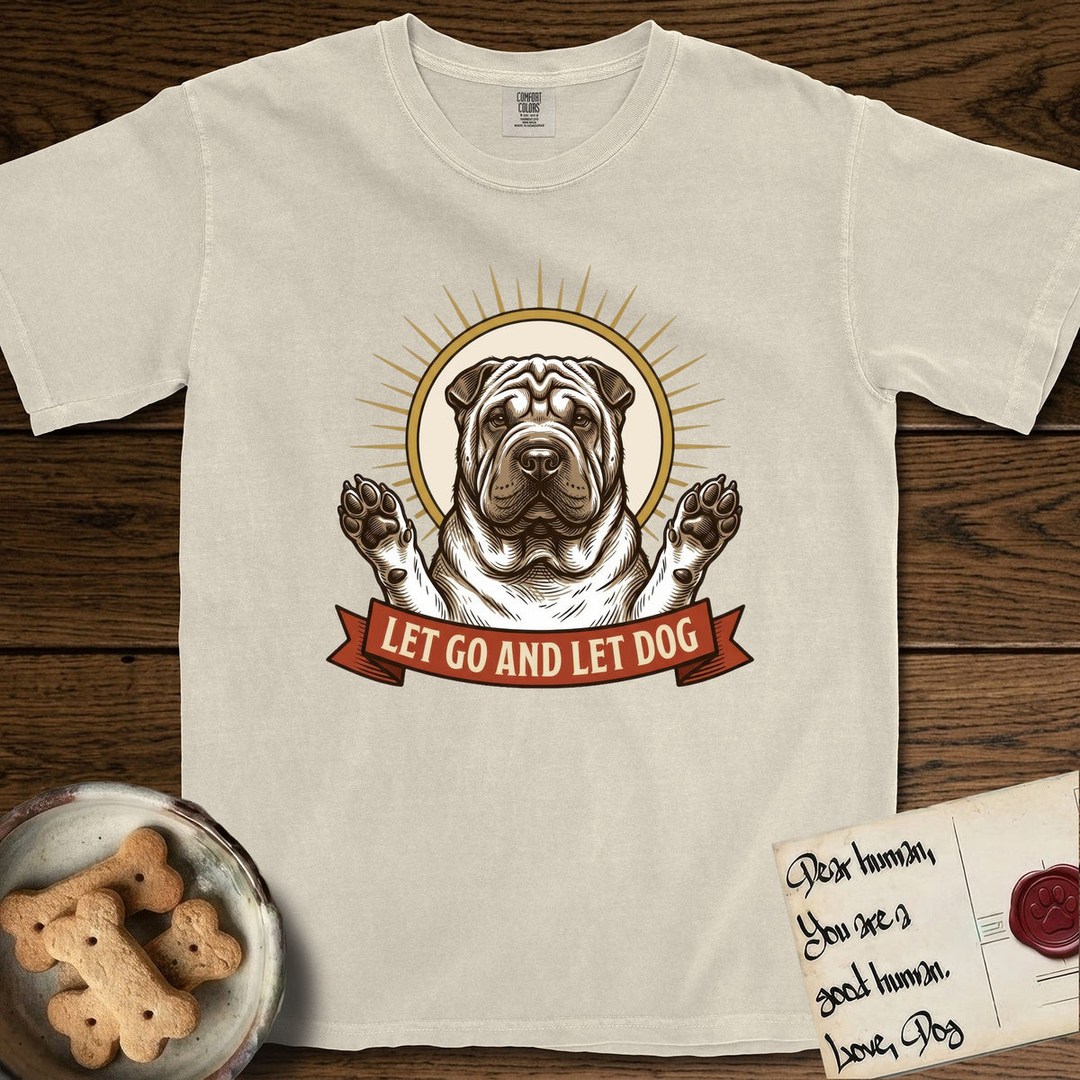 Let Go and Let Dog Shar-Pei T-Shirt flat lay in Ivory, featuring an engraved woodcut portrait of a haloed wrinkled Shar-Pei, paws raised, sunburst rays behind her and a ribbon banner below.