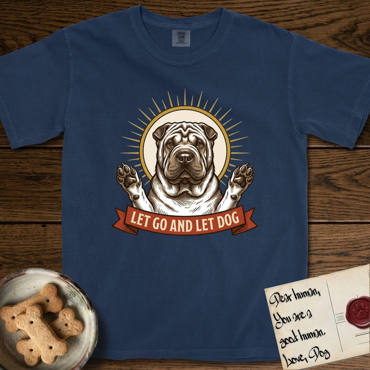 Let Go and Let Dog Shar-Pei T-Shirt flat lay in True Navy, featuring an engraved woodcut portrait of a haloed wrinkled Shar-Pei, paws raised, sunburst rays behind her and a ribbon banner below.