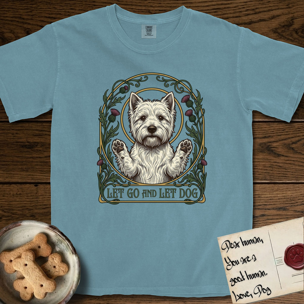 Let Go and Let Dog Westie T-Shirt flat lay in Ice Blue, featuring an Art Nouveau arch of thistles and curling vines around a haloed West Highland White Terrier, paws raised.