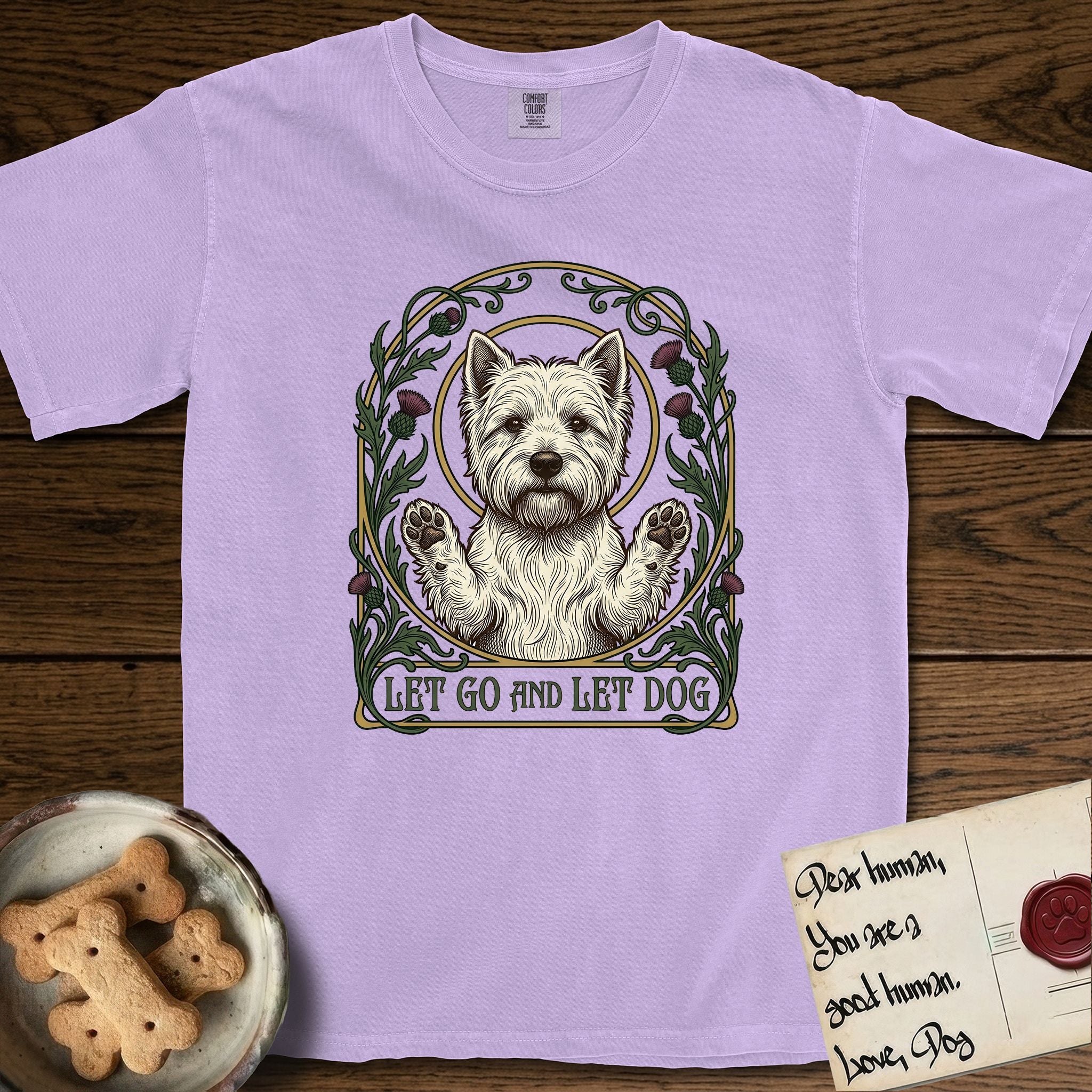 Let Go and Let Dog Westie T-Shirt flat lay in Orchid, featuring an Art Nouveau arch of thistles and curling vines around a haloed West Highland White Terrier, paws raised.