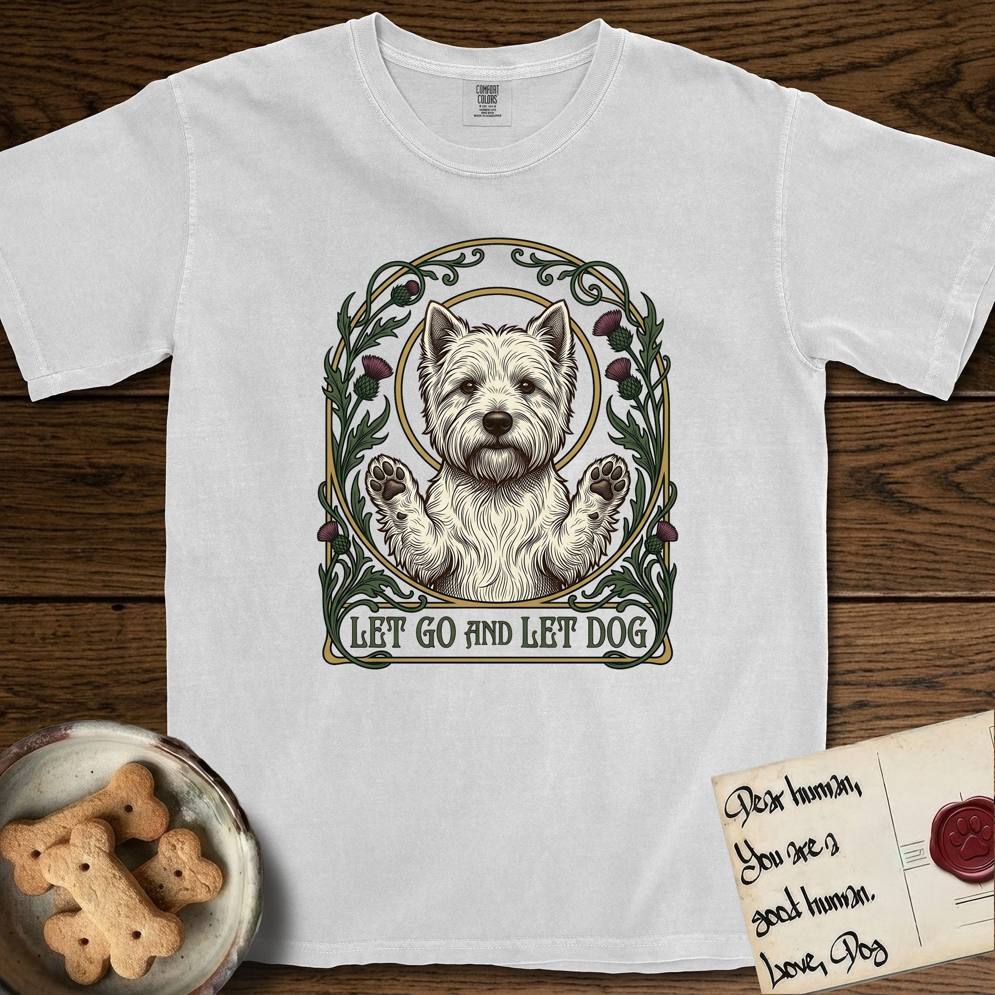 Let Go and Let Dog Westie T-Shirt flat lay in White, featuring an Art Nouveau arch of thistles and curling vines around a haloed West Highland White Terrier, paws raised.