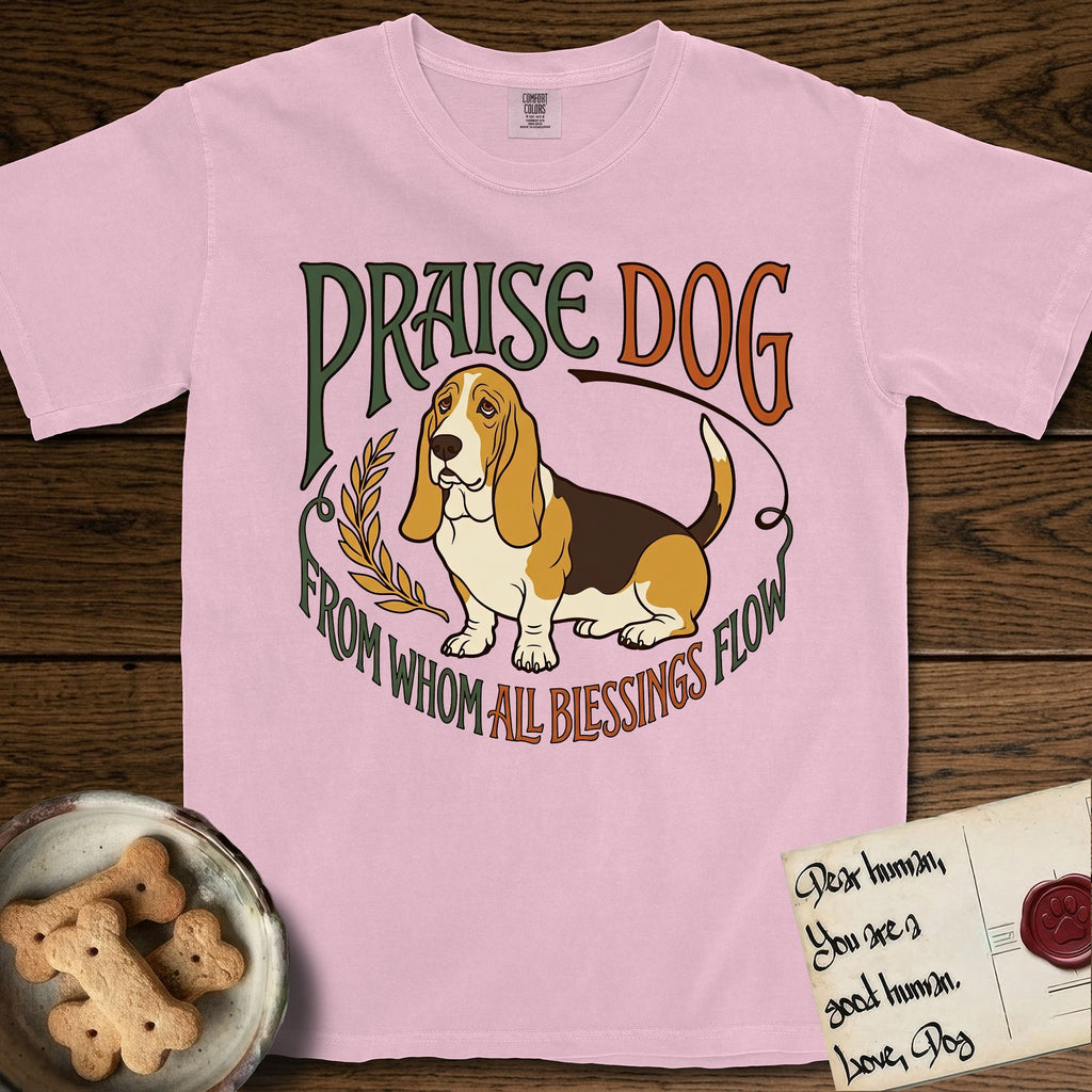 Praise Dog From Whom All Blessings Flow Basset Hound T-Shirt flat lay in Blossom, featuring an art nouveau hand-lettered design with a sad-eyed Basset Hound sitting beside a golden laurel sprig and the words Praise Dog From Whom All Blessings Flow.