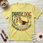 Praise Dog From Whom All Blessings Flow Basset Hound T-Shirt flat lay in Cornsilk, featuring an art nouveau hand-lettered design with a sad-eyed Basset Hound sitting beside a golden laurel sprig and the words Praise Dog From Whom All Blessings Flow.