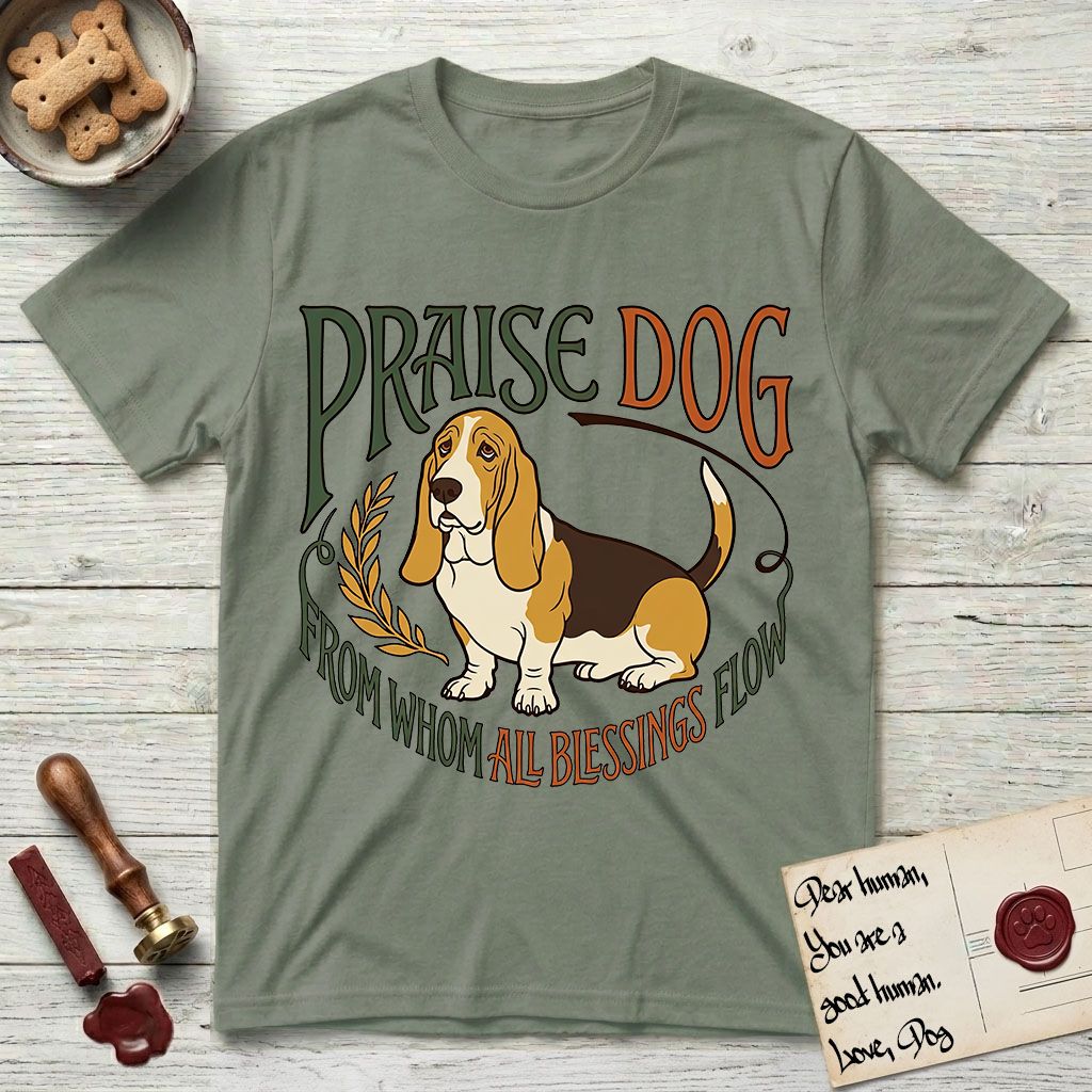 Praise Dog From Whom All Blessings Flow Basset Hound T-Shirt flat lay in Sage, featuring an art nouveau hand-lettered design with a sad-eyed Basset Hound sitting beside a golden laurel sprig and the words Praise Dog From Whom All Blessings Flow.