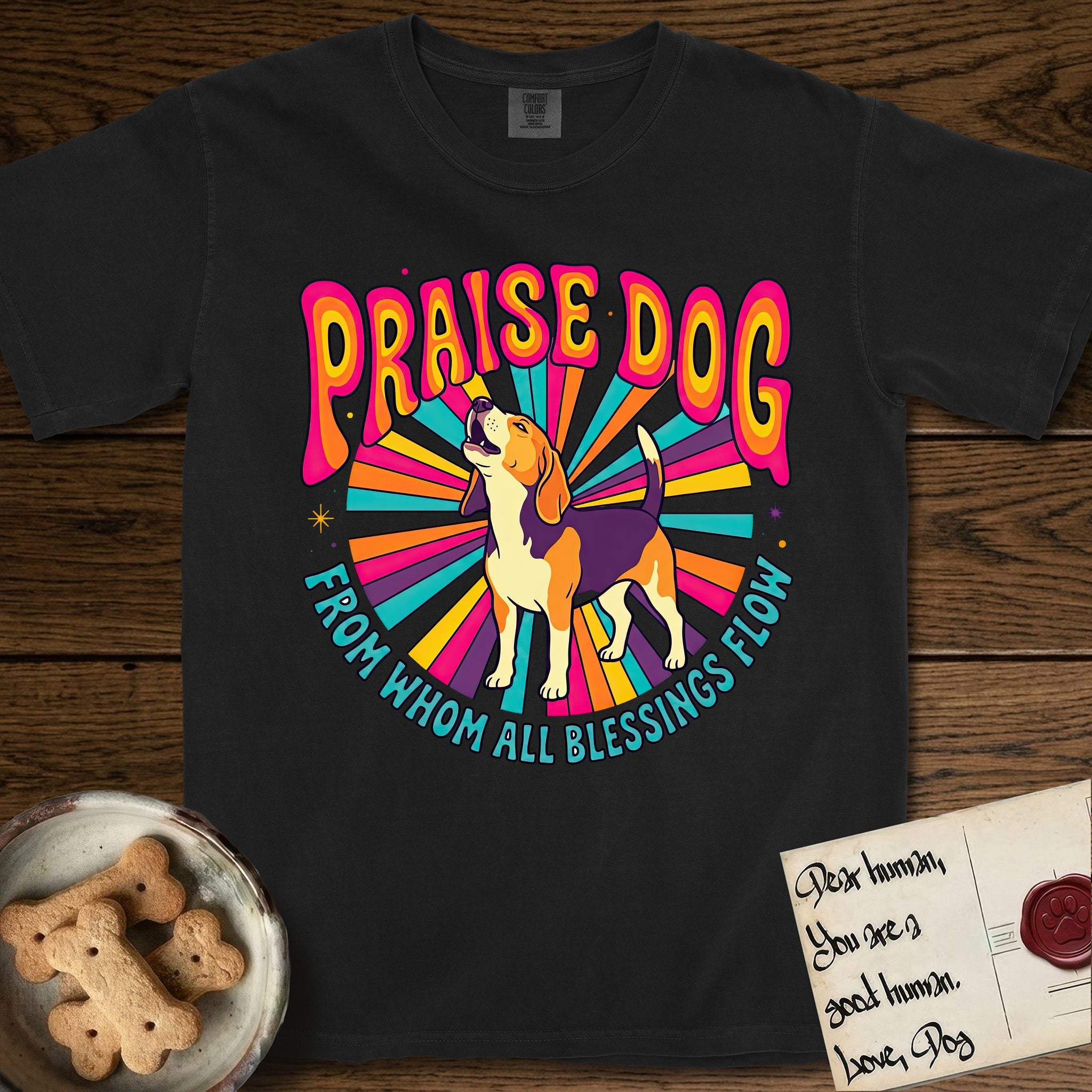 Praise Dog From Whom All Blessings Flow Beagle T-Shirt flat lay in Black, featuring a groovy psychedelic sunburst design with a Beagle howling skyward at the center and the words Praise Dog From Whom All Blessings Flow in rainbow bubble letters.