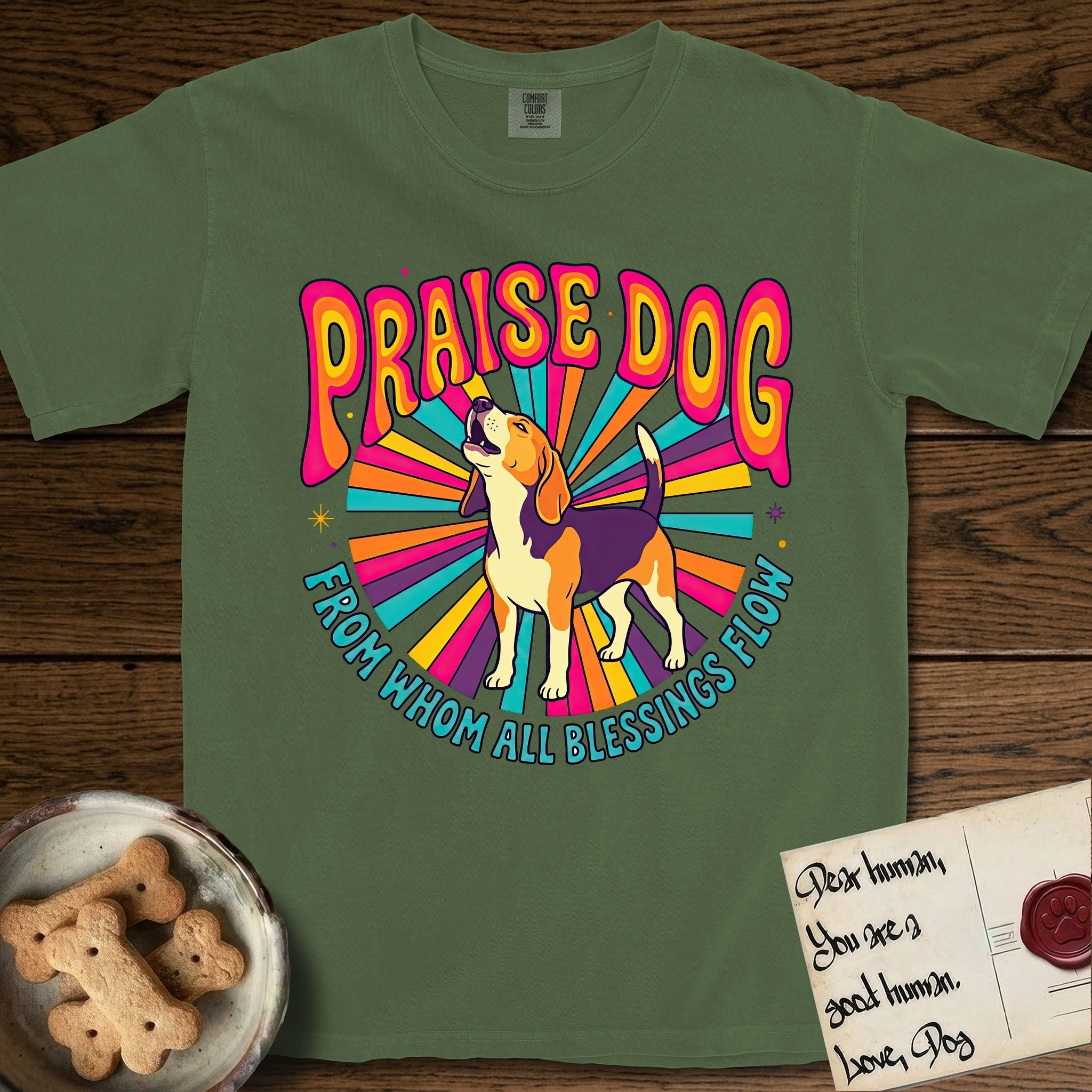 Praise Dog From Whom All Blessings Flow Beagle T-Shirt flat lay in Moss, featuring a groovy psychedelic sunburst design with a Beagle howling skyward at the center and the words Praise Dog From Whom All Blessings Flow in rainbow bubble letters.