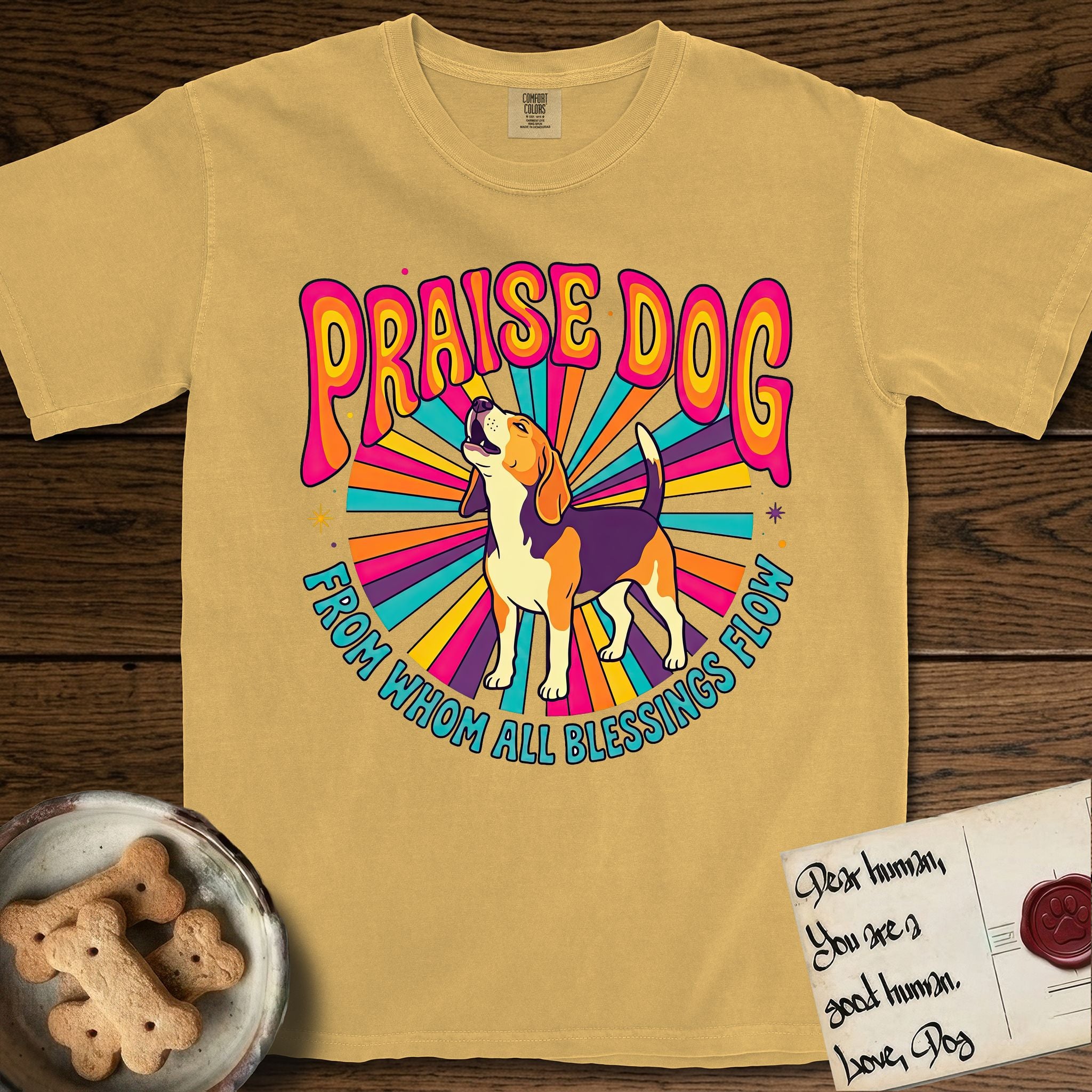 Praise Dog From Whom All Blessings Flow Beagle T-Shirt flat lay in Mustard, featuring a groovy psychedelic sunburst design with a Beagle howling skyward at the center and the words Praise Dog From Whom All Blessings Flow in rainbow bubble letters.