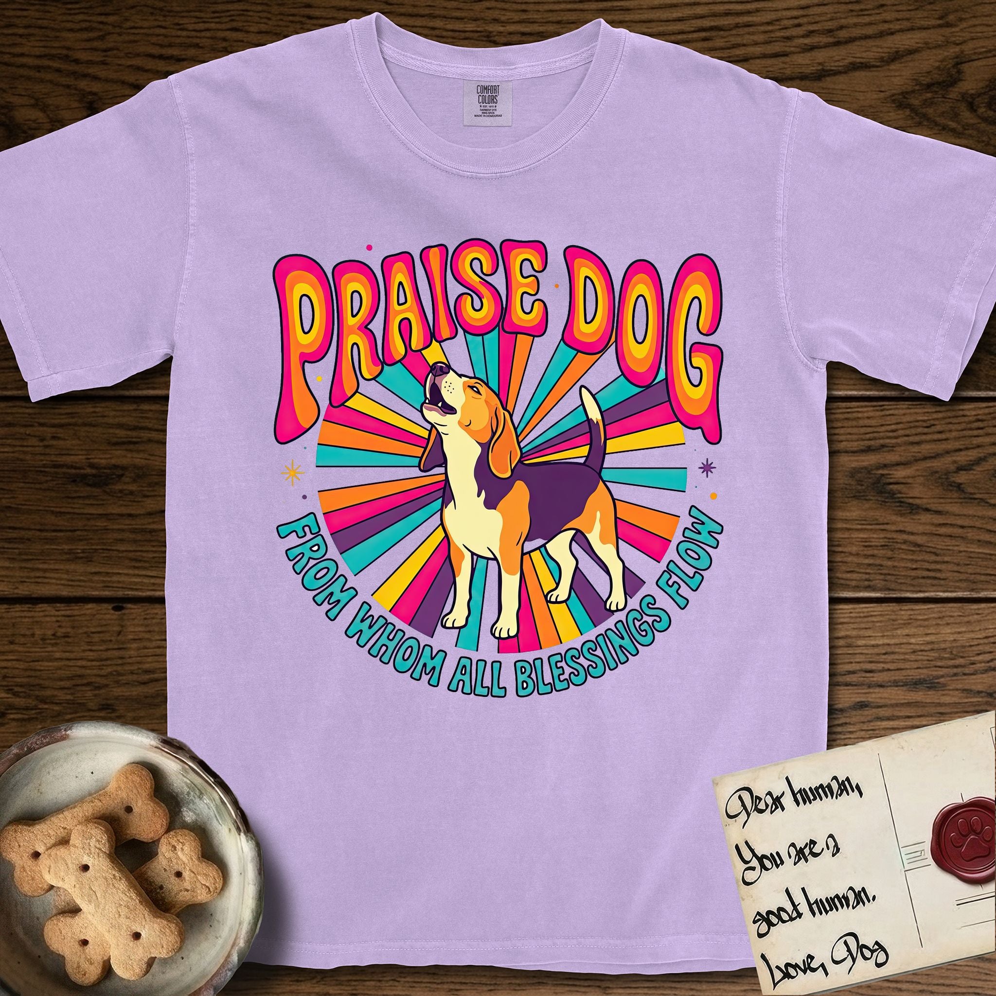 Praise Dog From Whom All Blessings Flow Beagle T-Shirt flat lay in Orchid, featuring a groovy psychedelic sunburst design with a Beagle howling skyward at the center and the words Praise Dog From Whom All Blessings Flow in rainbow bubble letters.