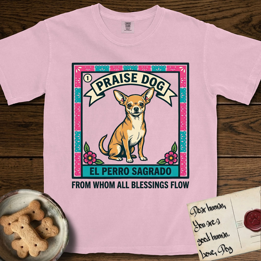 Praise Dog From Whom All Blessings Flow Chihuahua T-Shirt flat lay in Blossom, featuring a loteria-style folk art card with a Chihuahua seated inside a papel picado border, a banner reading El Perro Sagrado, and the words Praise Dog From Whom All Blessings Flow.