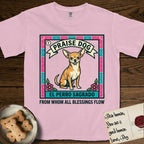 Praise Dog From Whom All Blessings Flow Chihuahua T-Shirt flat lay in Blossom, featuring a loteria-style folk art card with a Chihuahua seated inside a papel picado border, a banner reading El Perro Sagrado, and the words Praise Dog From Whom All Blessings Flow.