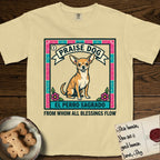 Praise Dog From Whom All Blessings Flow Chihuahua T-Shirt flat lay in Butter, featuring a loteria-style folk art card with a Chihuahua seated inside a papel picado border, a banner reading El Perro Sagrado, and the words Praise Dog From Whom All Blessings Flow.