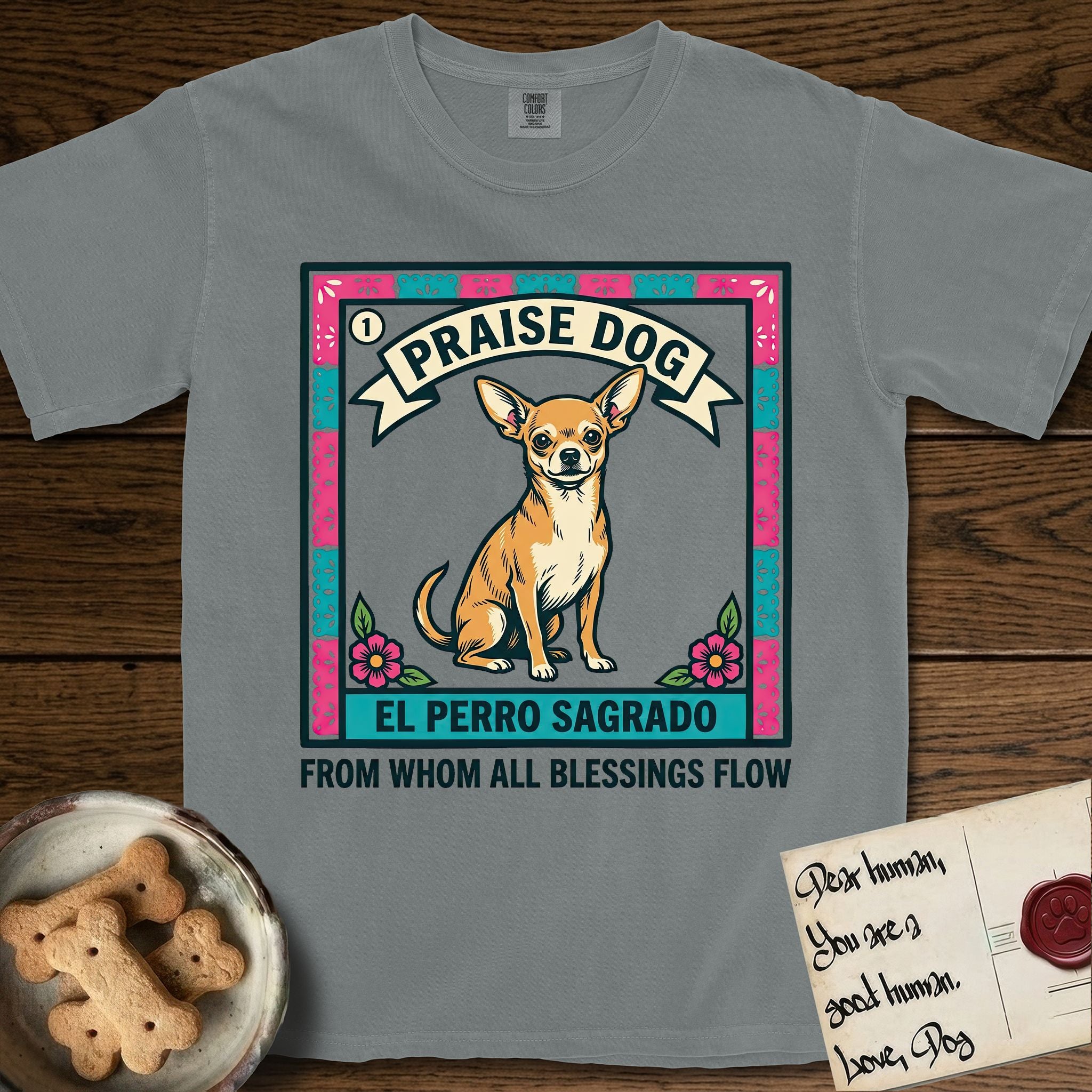 Praise Dog From Whom All Blessings Flow Chihuahua T-Shirt flat lay in Granite, featuring a loteria-style folk art card with a Chihuahua seated inside a papel picado border, a banner reading El Perro Sagrado, and the words Praise Dog From Whom All Blessings Flow.