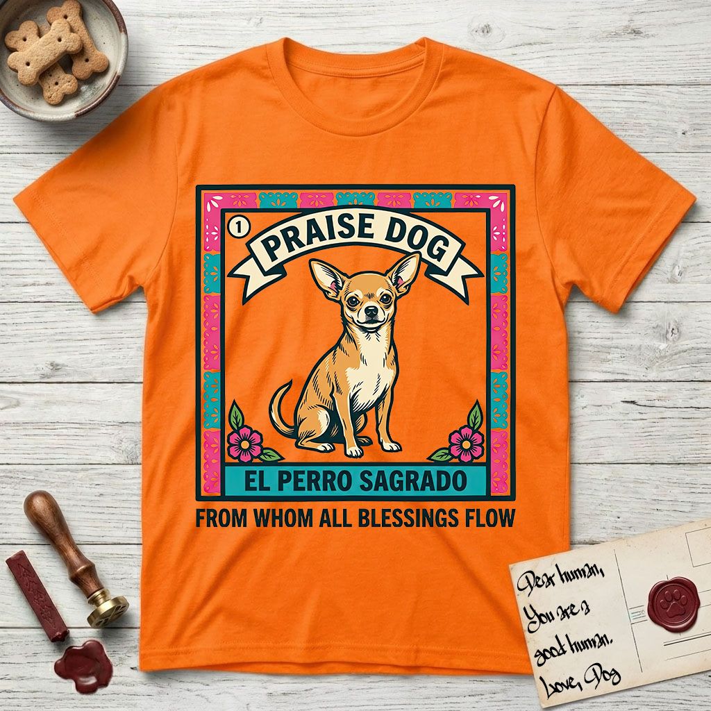 Praise Dog From Whom All Blessings Flow Chihuahua T-Shirt flat lay in Orange, featuring a loteria-style folk art card with a Chihuahua seated inside a papel picado border, a banner reading El Perro Sagrado, and the words Praise Dog From Whom All Blessings Flow.