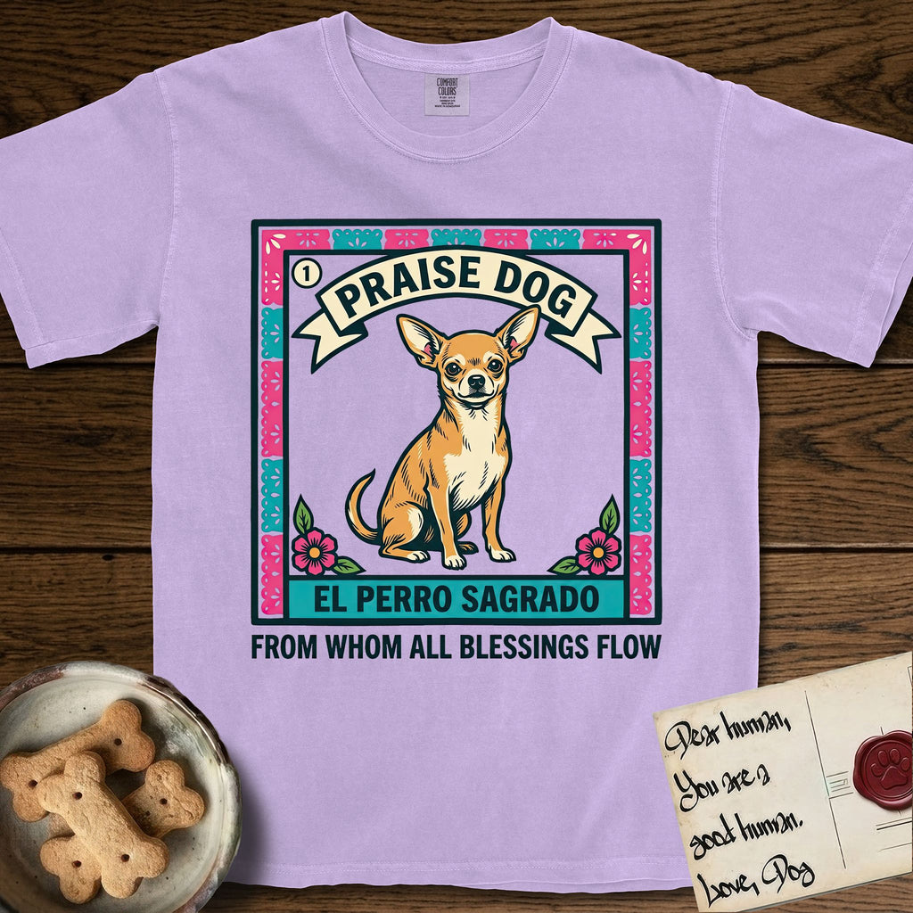 Praise Dog From Whom All Blessings Flow Chihuahua T-Shirt flat lay in Orchid, featuring a loteria-style folk art card with a Chihuahua seated inside a papel picado border, a banner reading El Perro Sagrado, and the words Praise Dog From Whom All Blessings Flow.
