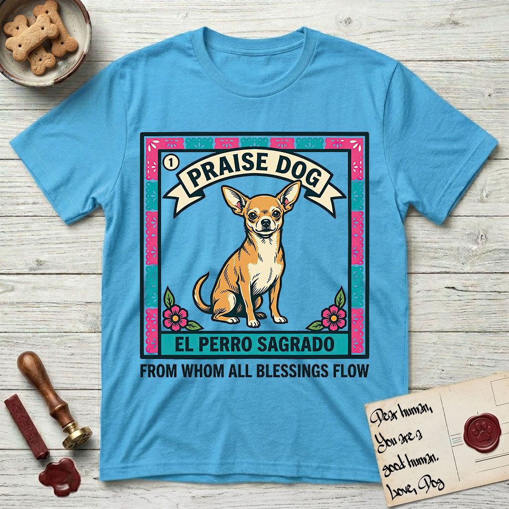Praise Dog From Whom All Blessings Flow Chihuahua T-Shirt flat lay in Sky, featuring a loteria-style folk art card with a Chihuahua seated inside a papel picado border, a banner reading El Perro Sagrado, and the words Praise Dog From Whom All Blessings Flow.
