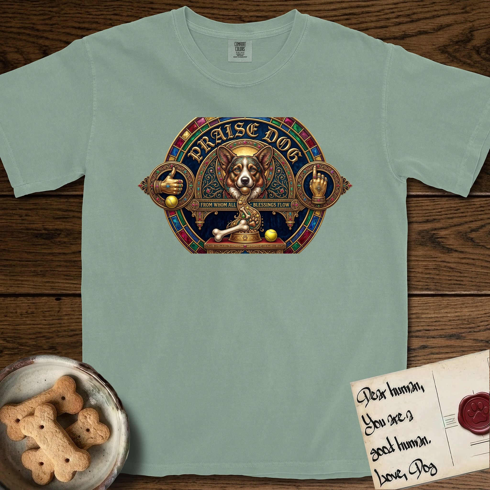 Praise Dog From Whom All Blessings Flow Corgi T-Shirt flat lay in Bay, featuring a jeweled baroque throne emblem with a Corgi at center, a golden gemstone frame, raised golden hands in blessing, and the words Praise Dog.