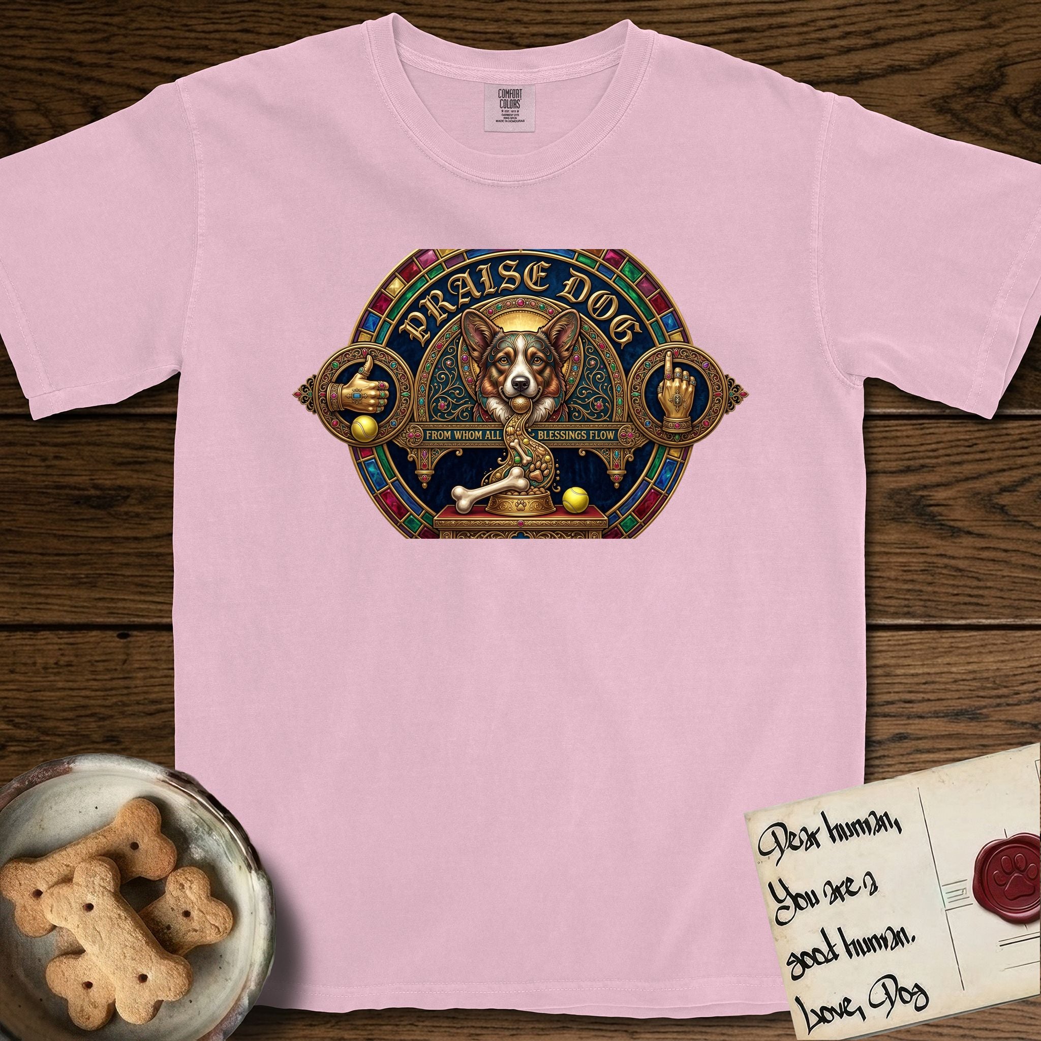 Praise Dog From Whom All Blessings Flow Corgi T-Shirt flat lay in Blossom, featuring a jeweled baroque throne emblem with a Corgi at center, a golden gemstone frame, raised golden hands in blessing, and the words Praise Dog.