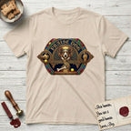 Praise Dog From Whom All Blessings Flow Corgi T-Shirt flat lay in Sand, featuring a jeweled baroque throne emblem with a Corgi at center, a golden gemstone frame, raised golden hands in blessing, and the words Praise Dog.