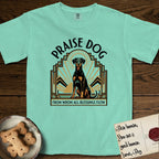 Praise Dog From Whom All Blessings Flow Doberman T-Shirt flat lay in Island Reef, featuring an Art Deco emblem of a seated Doberman with natural ears and full tail, framed by geometric gold and jade rays with a sunburst halo and "Praise Dog From Whom All Blessings Flow" lettering.