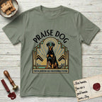 Praise Dog From Whom All Blessings Flow Doberman T-Shirt flat lay in Sage, featuring an Art Deco emblem of a seated Doberman with natural ears and full tail, framed by geometric gold and jade rays with a sunburst halo and "Praise Dog From Whom All Blessings Flow" lettering.