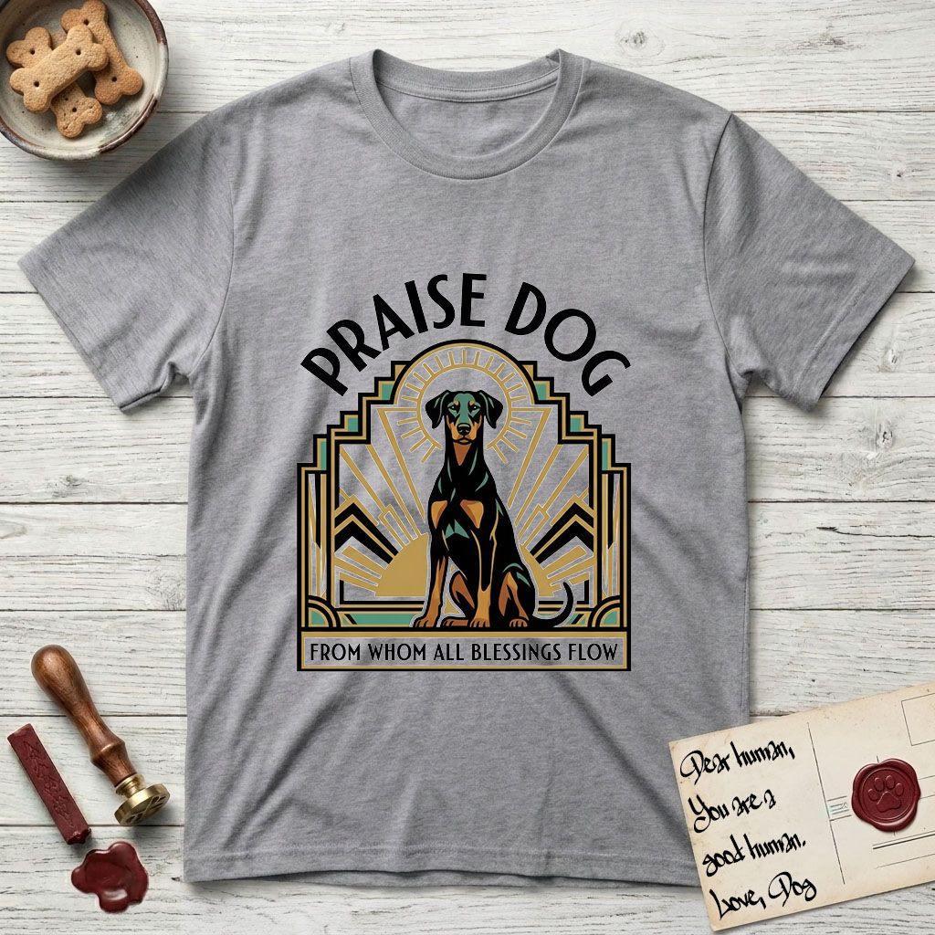 Praise Dog From Whom All Blessings Flow Doberman T-Shirt flat lay in Sport Grey, featuring an Art Deco emblem of a seated Doberman with natural ears and full tail, framed by geometric gold and jade rays with a sunburst halo and "Praise Dog From Whom All Blessings Flow" lettering.