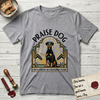Praise Dog From Whom All Blessings Flow Doberman T-Shirt flat lay in Sport Grey, featuring an Art Deco emblem of a seated Doberman with natural ears and full tail, framed by geometric gold and jade rays with a sunburst halo and "Praise Dog From Whom All Blessings Flow" lettering.
