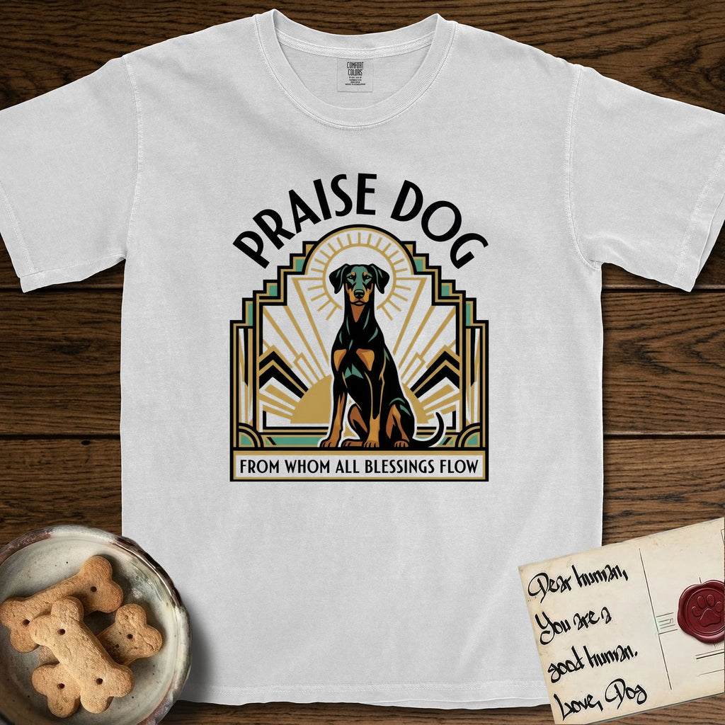 Praise Dog From Whom All Blessings Flow Doberman T-Shirt flat lay in White, featuring an Art Deco emblem of a seated Doberman with natural ears and full tail, framed by geometric gold and jade rays with a sunburst halo and "Praise Dog From Whom All Blessings Flow" lettering.