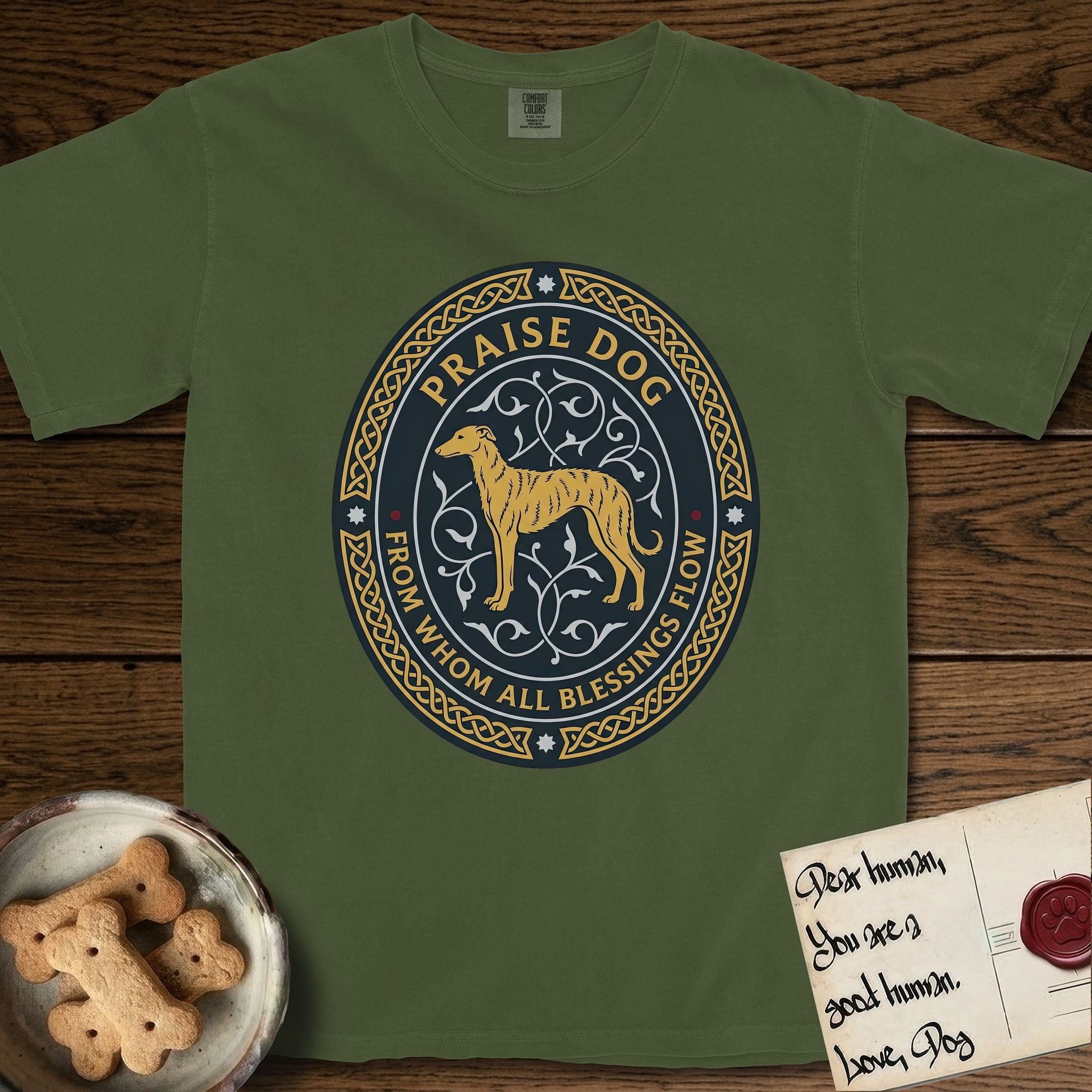 Praise Dog From Whom All Blessings Flow Galgo T-Shirt flat lay in Hemp, featuring a gold and navy oval medallion with a brindle Galgo standing in profile over silver filigree vines, a knotwork border, and the words Praise Dog From Whom All Blessings Flow.