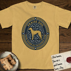 Praise Dog From Whom All Blessings Flow Galgo T-Shirt flat lay in Mustard, featuring a gold and navy oval medallion with a brindle Galgo standing in profile over silver filigree vines, a knotwork border, and the words Praise Dog From Whom All Blessings Flow.