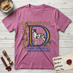 Praise Dog From Whom All Blessings Flow Great Dane T-Shirt flat lay in Heather Radiant Orchid, featuring an illuminated manuscript capital D in blue and gold with a harlequin Great Dane standing inside the letter and the words Praise Dog From Whom All Blessings Flow.