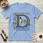Praise Dog From Whom All Blessings Flow Great Dane T-Shirt flat lay in Light Blue, featuring an illuminated manuscript capital D in blue and gold with a harlequin Great Dane standing inside the letter and the words Praise Dog From Whom All Blessings Flow.