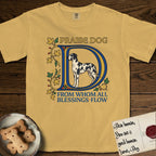 Praise Dog From Whom All Blessings Flow Great Dane T-Shirt flat lay in Mustard, featuring an illuminated manuscript capital D in blue and gold with a harlequin Great Dane standing inside the letter and the words Praise Dog From Whom All Blessings Flow.