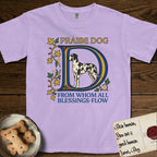 Praise Dog From Whom All Blessings Flow Great Dane T-Shirt flat lay in Orchid, featuring an illuminated manuscript capital D in blue and gold with a harlequin Great Dane standing inside the letter and the words Praise Dog From Whom All Blessings Flow.