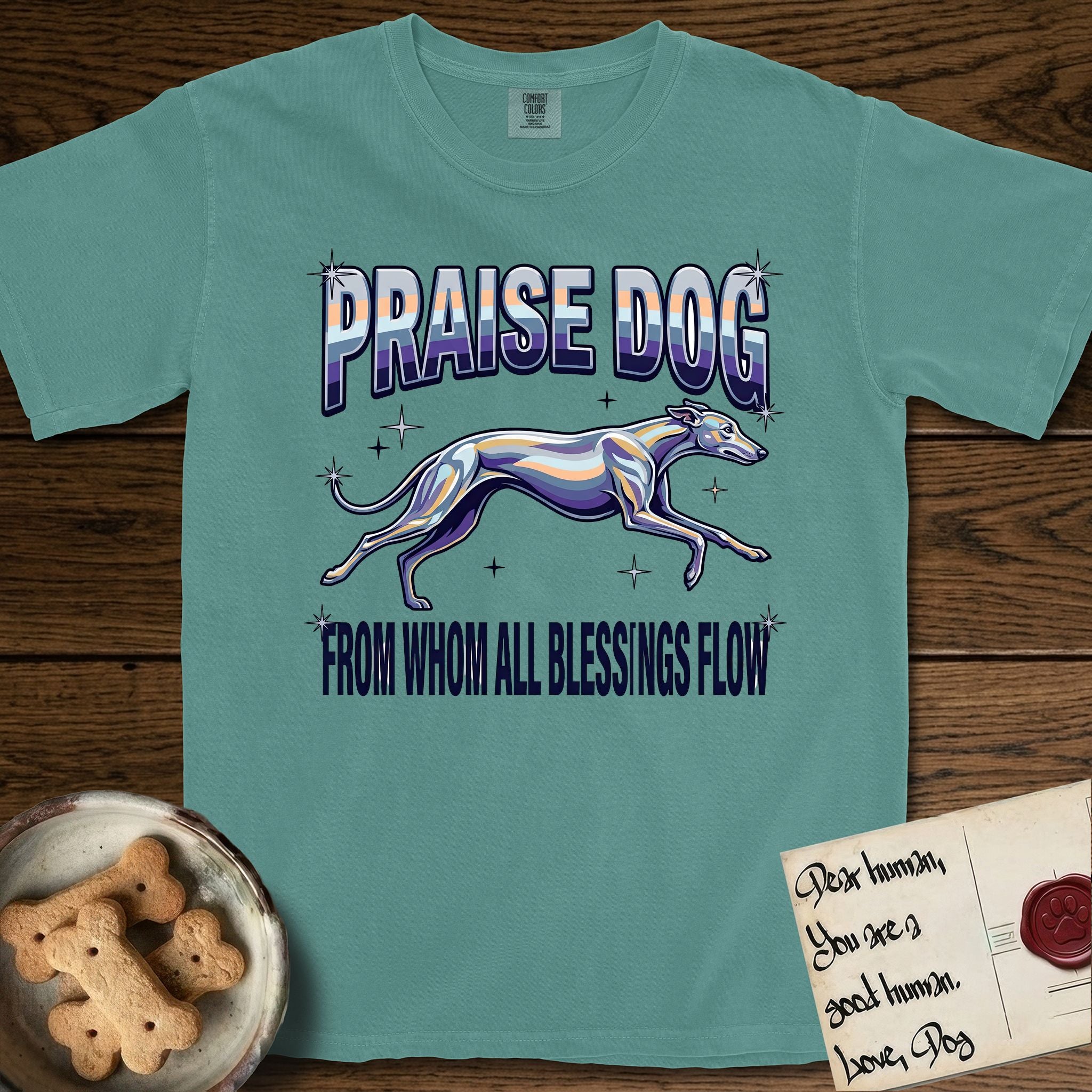 Praise Dog From Whom All Blessings Flow Greyhound T-Shirt flat lay in Blue Spruce, featuring a retro chrome airbrush design with a Greyhound running at full stretch among sparkle stars and the words Praise Dog From Whom All Blessings Flow in chrome sunset lettering.