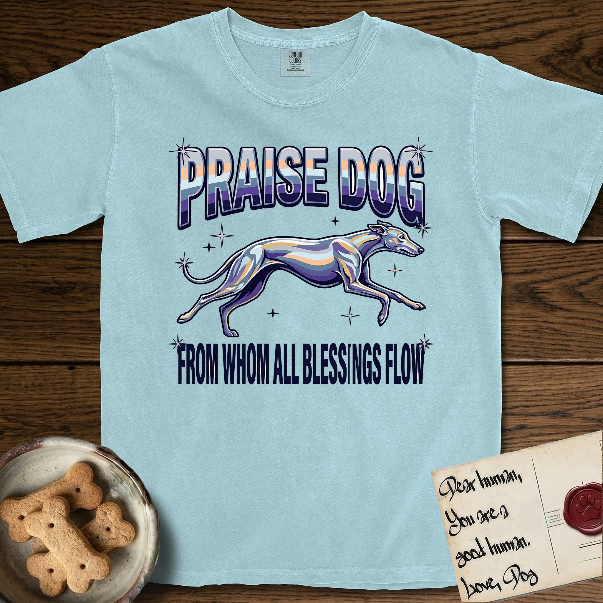 Praise Dog From Whom All Blessings Flow Greyhound T-Shirt flat lay in Chambray, featuring a retro chrome airbrush design with a Greyhound running at full stretch among sparkle stars and the words Praise Dog From Whom All Blessings Flow in chrome sunset lettering.