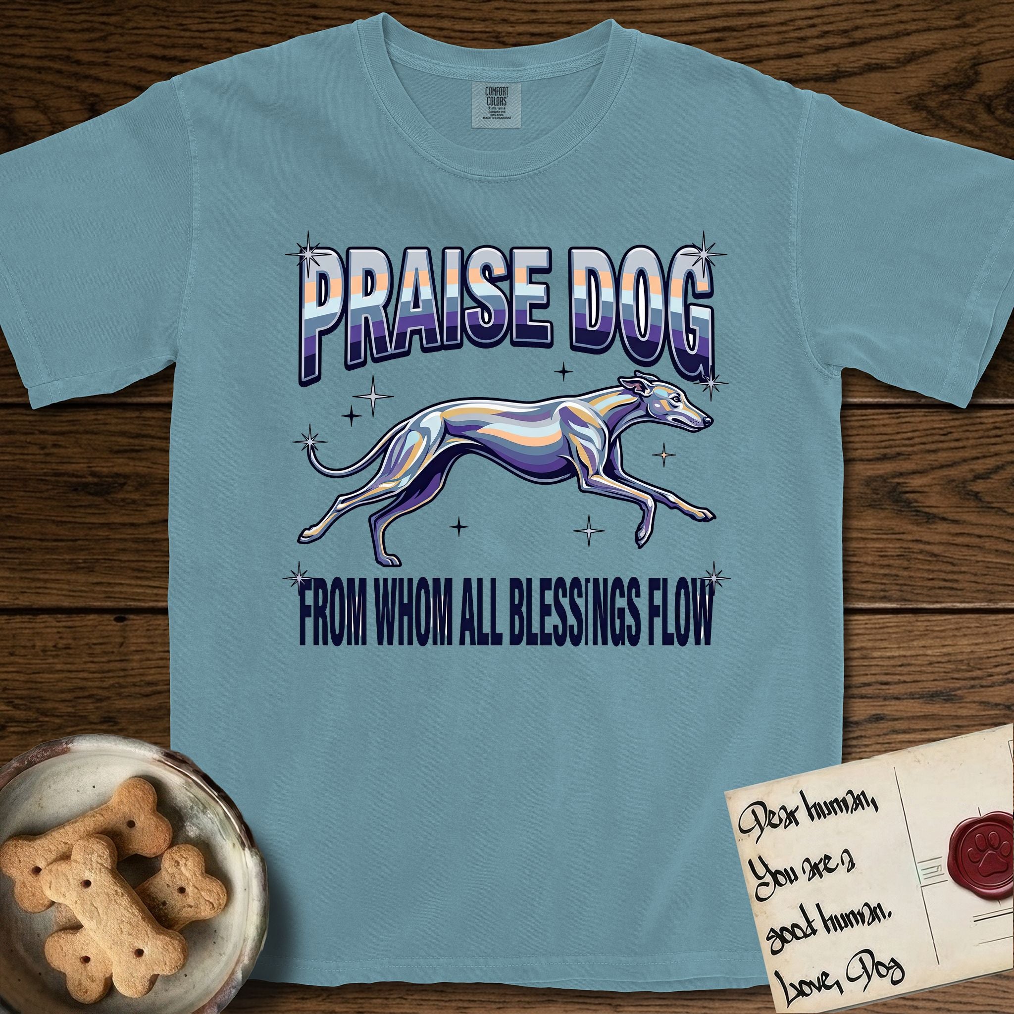 Praise Dog From Whom All Blessings Flow Greyhound T-Shirt flat lay in Ice Blue, featuring a retro chrome airbrush design with a Greyhound running at full stretch among sparkle stars and the words Praise Dog From Whom All Blessings Flow in chrome sunset lettering.