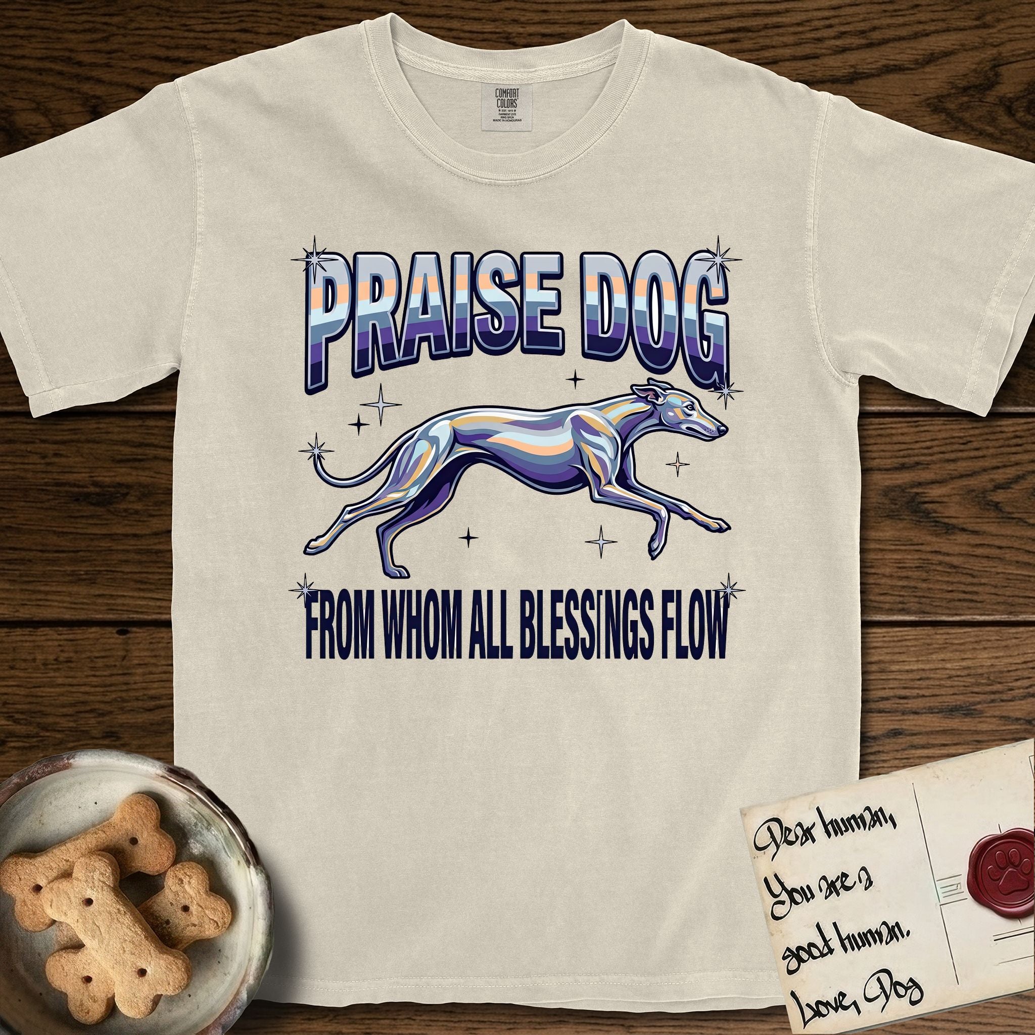 Praise Dog From Whom All Blessings Flow Greyhound T-Shirt flat lay in Ivory, featuring a retro chrome airbrush design with a Greyhound running at full stretch among sparkle stars and the words Praise Dog From Whom All Blessings Flow in chrome sunset lettering.